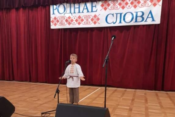 Zdjęcie przedstawia chłopca stojącego przed mikrofonem podczas recytacji wiersza.
