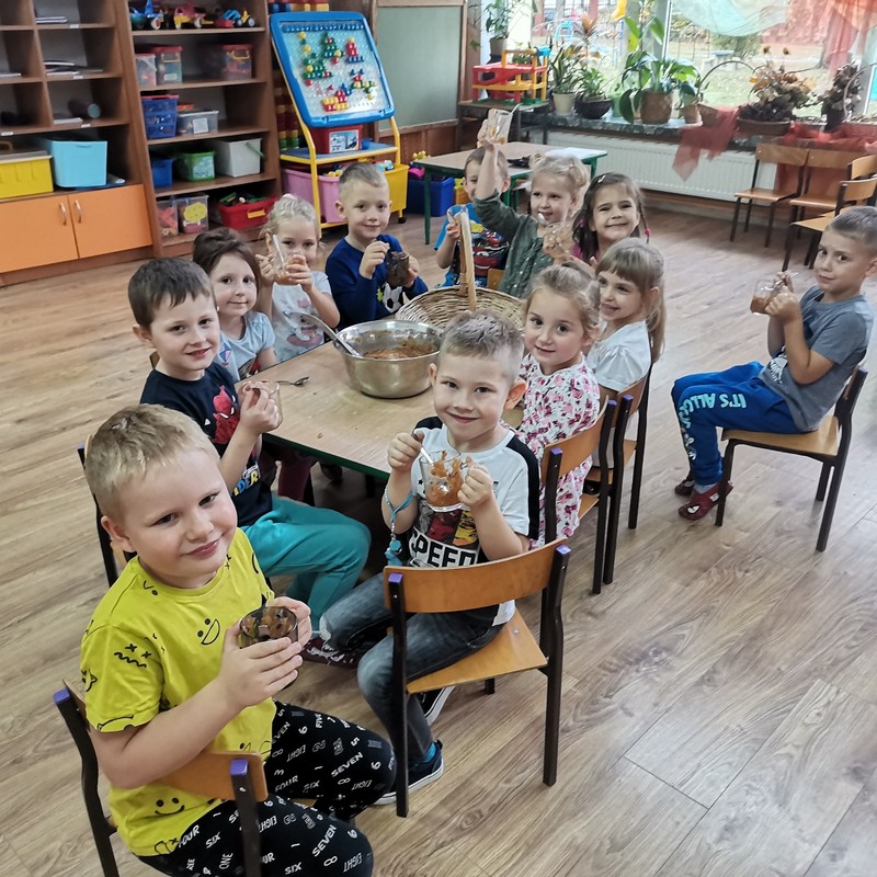 Dzieci z grupy Jaskółki siedzą przy stole, jedzą własnoręcznie przygotowany deser owocowy.
