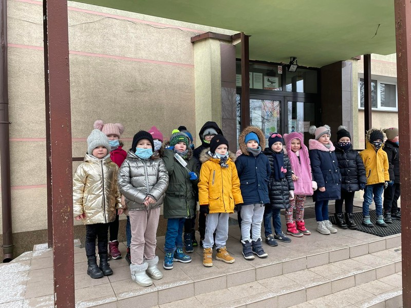 Grupka dzieci stoi przed wejściem do Szkoły Podstawowej Numer 1