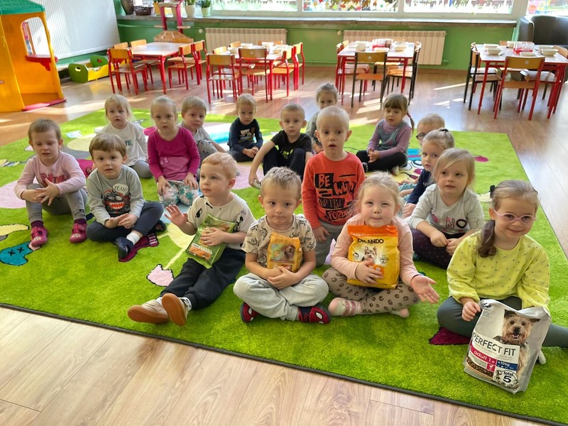 Grupa dzieci siedząca na dywanie w przedszkolnej sali.