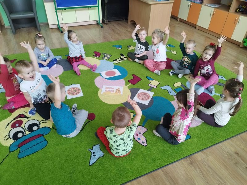 Dzieci siedzące na dywanie w przedszkolnej sali.