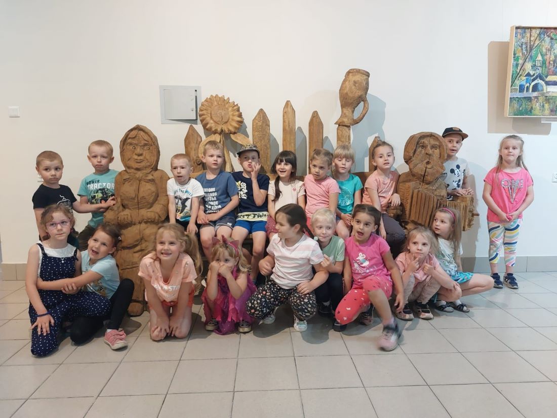 grupa dzieci pozuje do zdjecia przy drewnianych rzeźbach