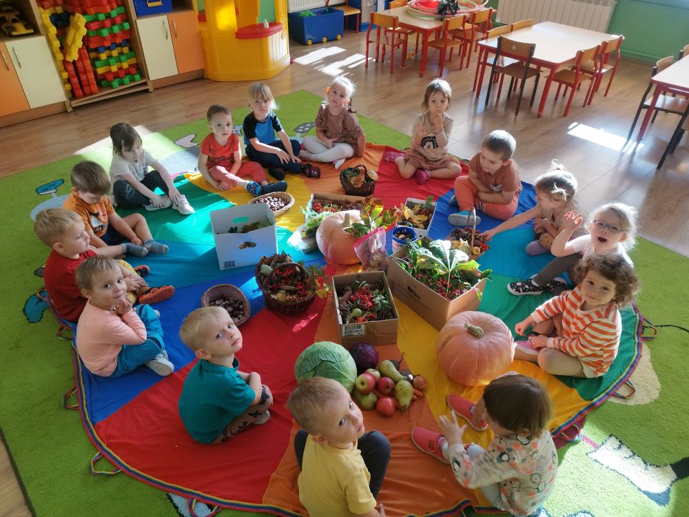 dzieci siedzą na ogrągłym dywanie. W środku leżą jesienne skarby.