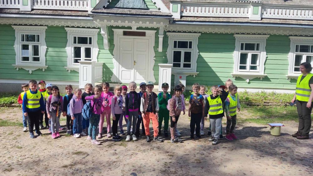 Duża grupa dzieci i kobieta przed budynkiem Ośrodka Edukacji Przyrodniczej w Białowieży
