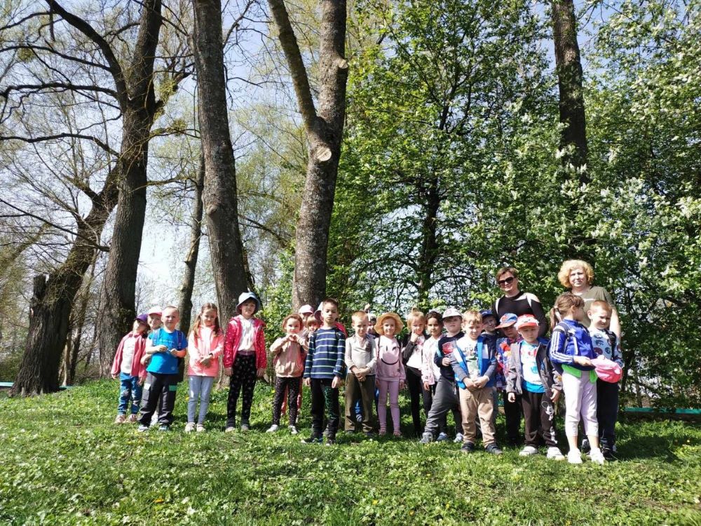 Przedszkolaki z wychowawczynią i Panią Leśnik stojąją w plenerze Białowieskiego Parku Narodowego. 